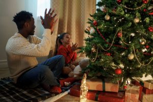 a father and daughter sit by a christmas tree