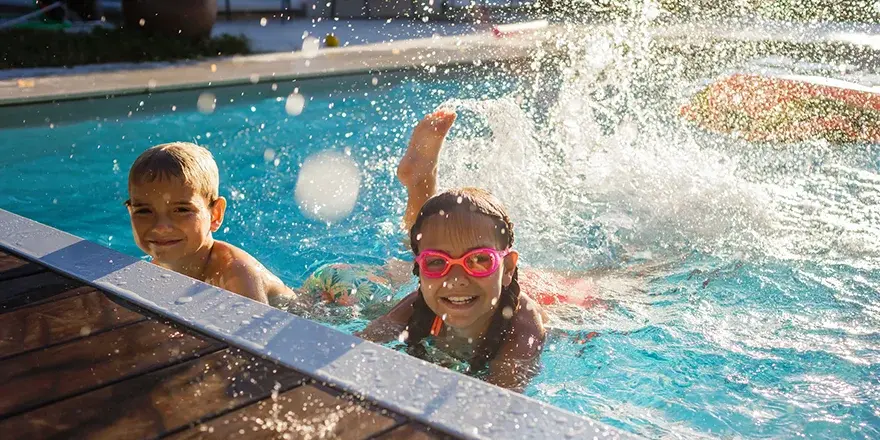 two children swimming in a blue pool, and using their feet to splash the water behind them