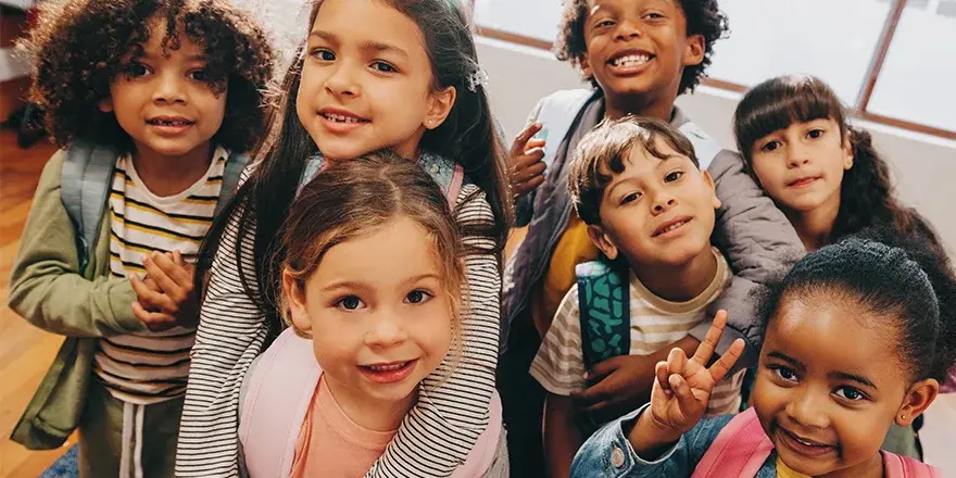 A group of grammar school children wearing backpacks standing close together at school.